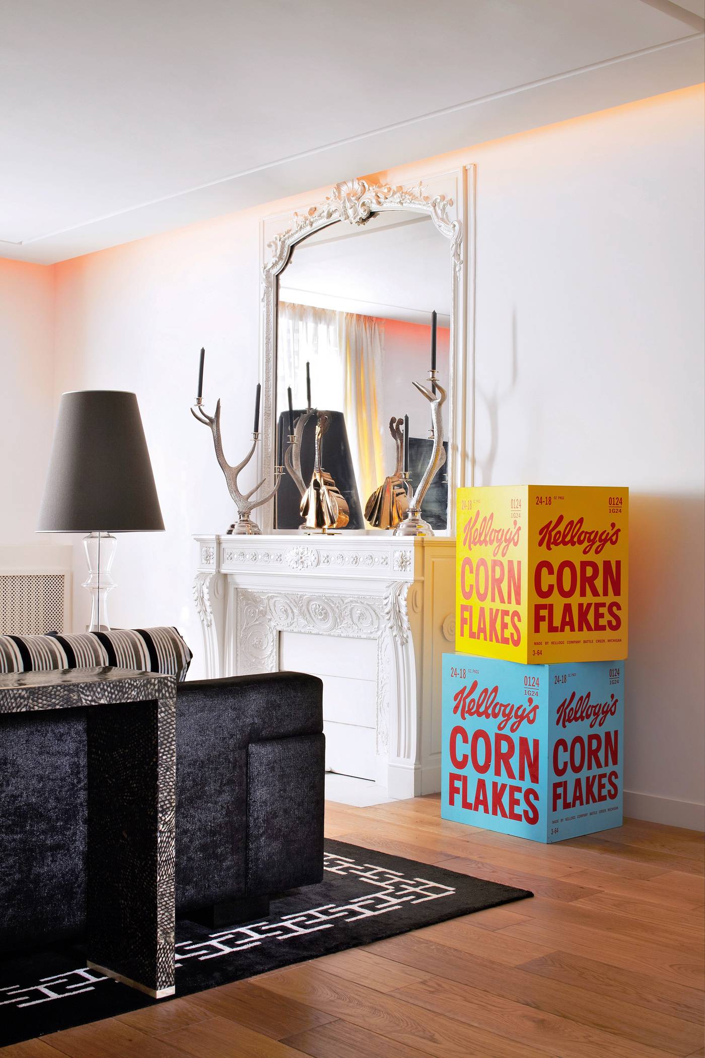L’architecte d’intérieur Stéphanie Coutas a conservé la belle cheminée d’origine ; bougeoirs aux lignes élancées (Mellerio). Le tapis noir Pierre Frey/ Braquenié contraste avec les cubes Kellogg’s en acrylique sur bois, pièces uniques de Cédric Avril.