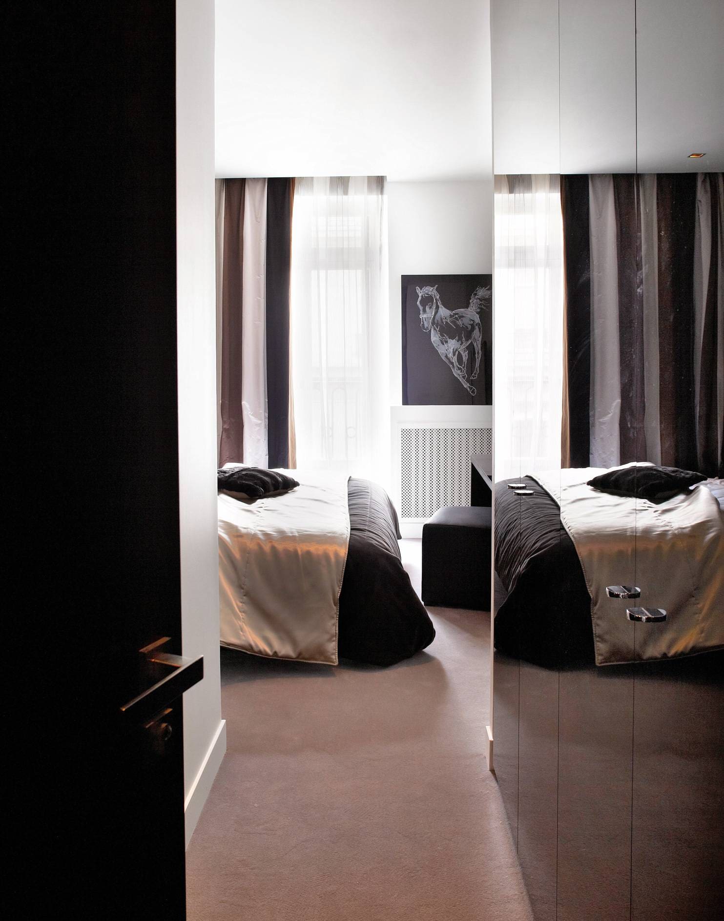 Dans une suite parentale, ambiance moirée reflétée par les portes du placard sur-mesure Quadro, couvre-lit Elitis ; pouf carré Marina Sièges, rideaux et coussins de (Designers Guild), tapis Bomat.